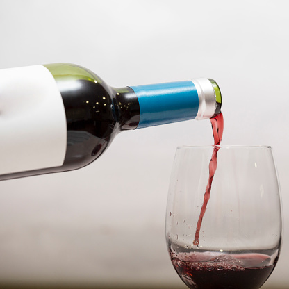 A closeup of red wine being poured in a wine glass against a white background.