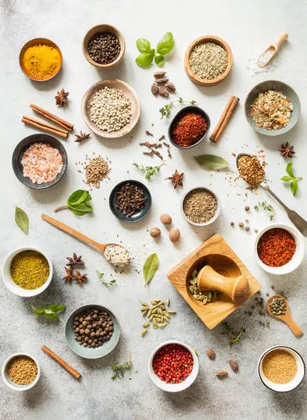 Various dry spices in small bowls and raw herbs flat lay on grey background. Top view