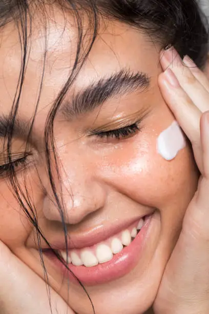 Close up studio shot of a beautiful woman with perfect skin, she applying cream at cheek.