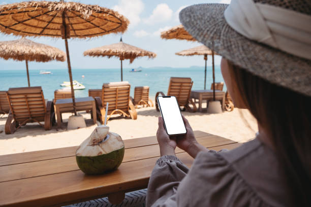 istock a woman holding mobile phone with blank desktop screen while sitting on the beach 1312114368