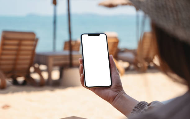 istock a woman holding mobile phone with blank desktop screen while sitting on the beach 1312114610