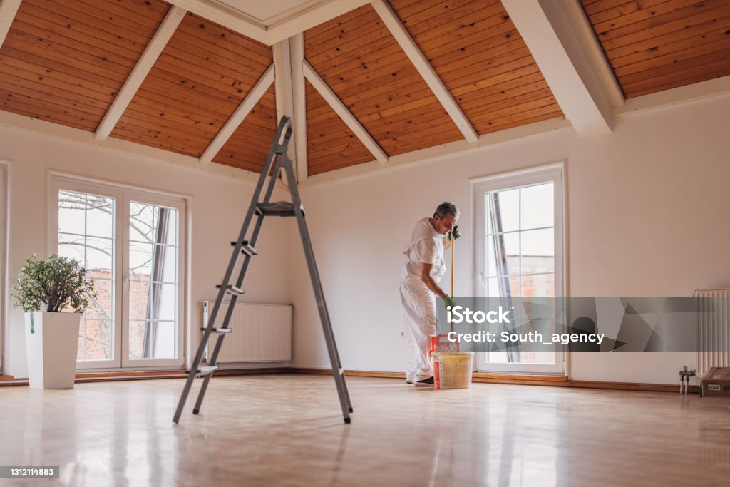 Mature painter painting a wall One man, mature male painter painting a wall with paint roller, indoors in a house. Painting - Activity Stock Photo