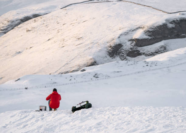 istock Winter mountain climber in red coat on white snow covered mountain hill taking break to keep warm eat and drink 1312118548