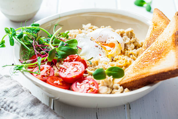 istock Savory oatmeal with poached egg, tomatoes, cheese and sprouts in white bowl. Healthy breakfast concept. 1312123300