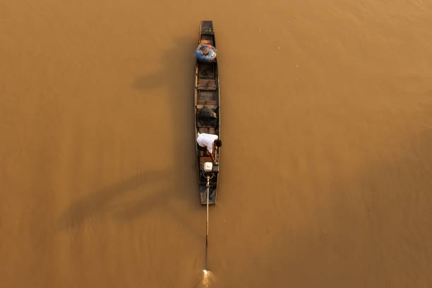 Aerial view an Asian fisherman stands on traditional wooden fishing boat while casting fishing net on a river at sunrise. Rural scene in Thailand. Focus on fisherman.