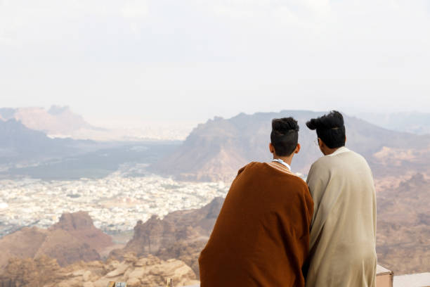Al Ula, Saudi Arabia, February 19 2020: Two Saudi Arabian youths look from a viewpoint in the mountains towards the Al Ula oasis in Saudi Arabia