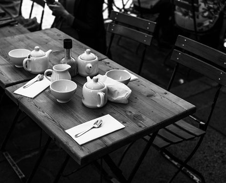 Teapots and teacups on wooden table in London restaurant, black and white