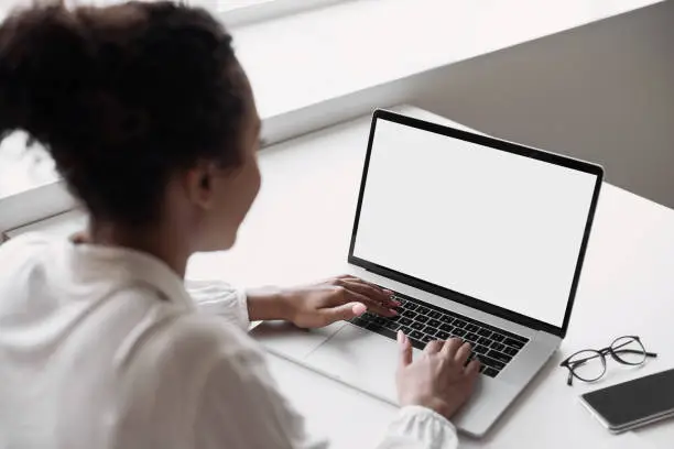 Photo of Young woman using laptop in office, white blank empty screen mock up
