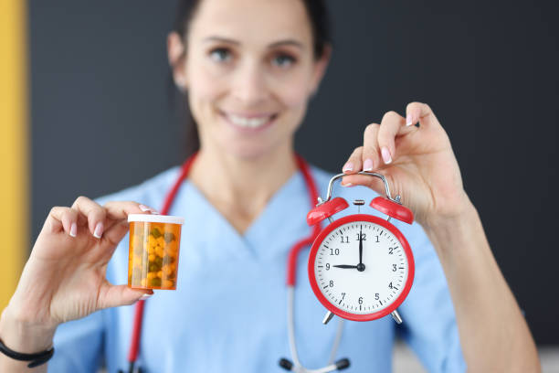 smiling doctor holds red alarm clock and medication in his hand - vitamin pill capsule equipment data imagens e fotografias de stock