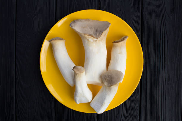 Mushrooms eringi in the yellow plate on the black wooden background