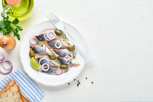 istock Salted herring with spice, herbs and onion on white plate on light stone background with copy space. Marinated sliced fish. Food with healthy unsaturated fats, flat lay 1312131029