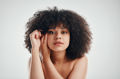 Studio shot of a beautiful young woman applying mascara against a grey background