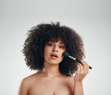 Studio shot of a young woman applying cosmetics against a grey background