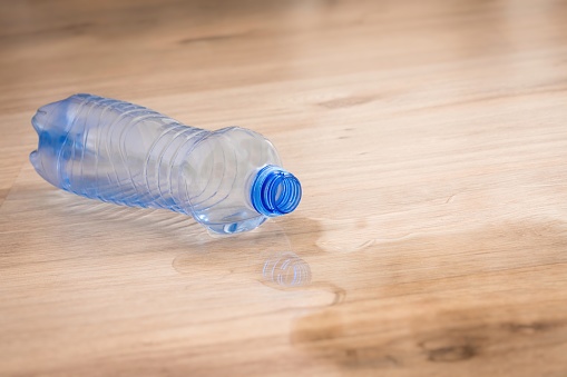 Spilled water and fallen plastic bottle on wooden laminate floor