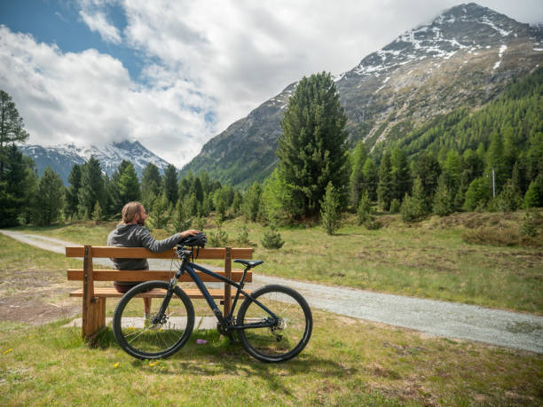 istock Mountain biker relaxes on bench, looks out view 1312134743