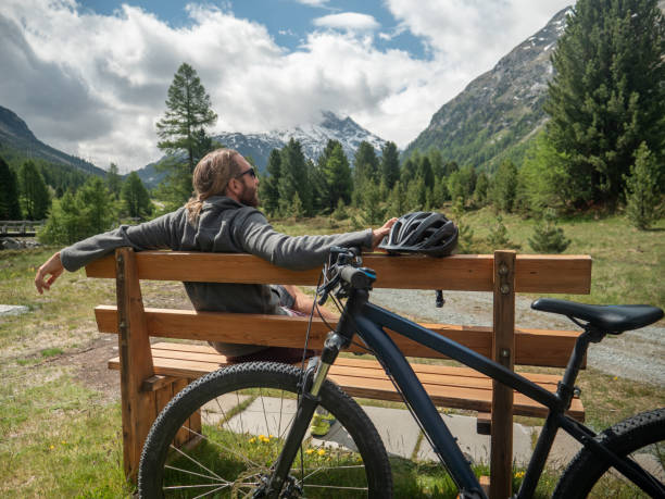 istock Mountain biker relaxes on bench, looks out view 1312135399