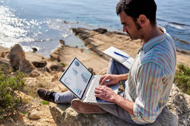 Photo of A young man works remotely with the sea in the background