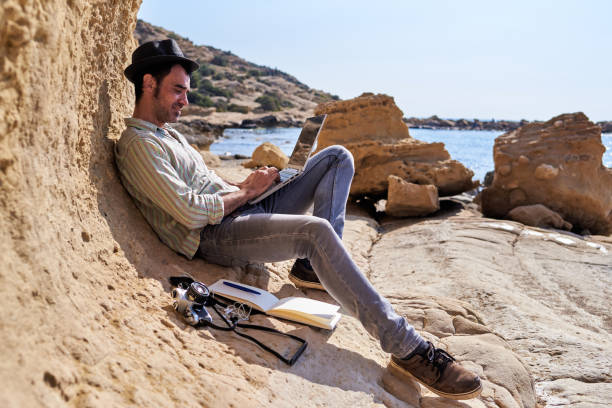 un joven escritor trabaja con su portátil desde la playa - only men mid adult men men author fotografías e imágenes de stock