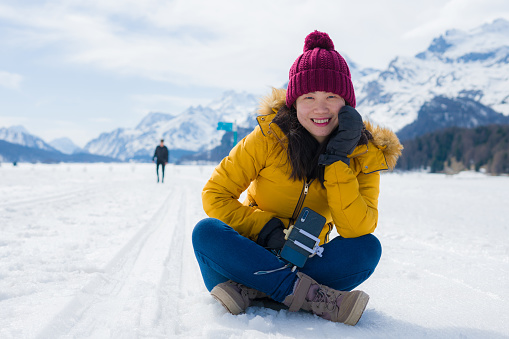 Winter holiday trip to snow valley - young happy and excited Asian Chinese woman playful on frozen lake in snowy mountains at Swiss Alps enjoying unique landscape