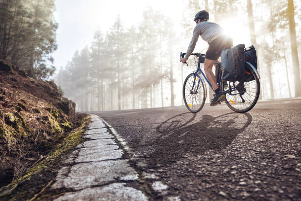 Cyclist on a bicycle with panniers riding along a foggy forest road stock photo