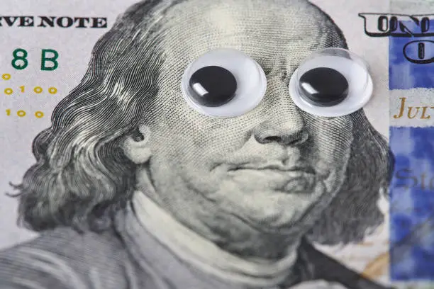 Photo of Fun Benjamin Franklin portrait with googly eyes, close-up of one hundred dollar bill.