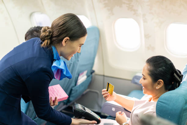 Onboard product purchasing, Asian woman sitting in airplane buying gift from air hostess and paying by credit card tapping on machine. Contactless payment and technology inflight service concept. Onboard product purchasing, Asian woman sitting in airplane buying gift from air hostess and paying by credit card tapping on machine. Contactless payment and technology inflight service concept. aboard stock pictures, royalty-free photos & images