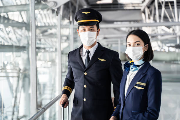 airliner pilot and air hostess wearing face mask walking in airport terminal to the airplanel during the covid pandemic to prevent coronavirus infection. new normal lifestyle in air transport concept. - cabin crew pilot airport walking imagens e fotografias de stock