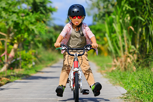 Country cycling walk. Young rider kid in helmet and sunglasses riding bicycle. Happy child have fun on empty trail. Active family lifestyle, sports, outdoor recreational activities on summer holidays.