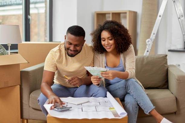 couple with blueprint counting money at home mortgage, moving and real estate concept - happy african american couple with blueprint and calculator counting money for repair costs to new home home improvement stock pictures, royalty-free photos & images