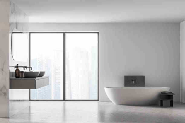 istock Front view of modern bathroom with double sink and white bathtub, large panoramic window, city view, minimalistic marble and concrete interior design. 1312143900
