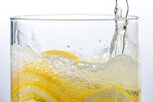 Close-up of pouring water to transparent glass. Bubbles in sparkling water. Homemade lemonade, source of vitamins, healthy lifestyle concept.