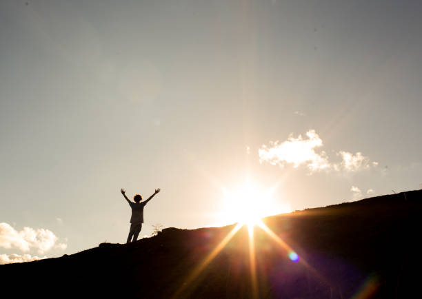 Never give up on your goals. Man with arms raised after climbing a mountain, with the sun in the background. Concept of not giving up on success and dreams or freedom, success and happiness never stock pictures, royalty-free photos & images