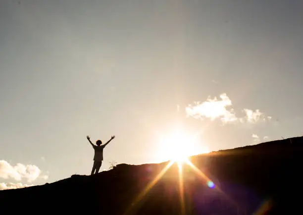 Man with arms raised after climbing a mountain, with the sun in the background. Concept of not giving up on success and dreams or freedom, success and happiness