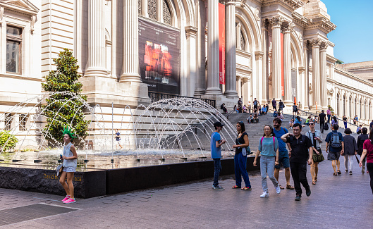 New York City, United States - August 26, 2017: Facade of the Metropolitan Museum of Art, with fountain, and people walking.