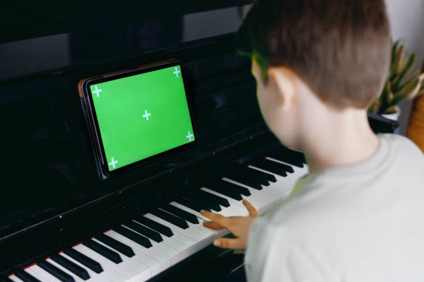 学校の少年学習タブレットアプリでピアノを再生します。子供は楽器を演奏することを学んで楽しんでいます。新しいアプリ、コマースやプログラムのための緑の画面のクロマキーの背景を� - piano keyboard instrument one person piano key ストックフォトと画像