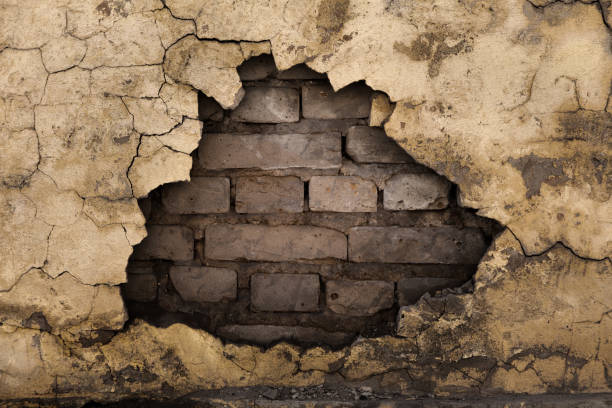 A gap in an old brick wall with fallen plaster Old damaged brick wall under plaster with cracks. Dark grunge texture background of old cement plaster collapsing stock pictures, royalty-free photos & images