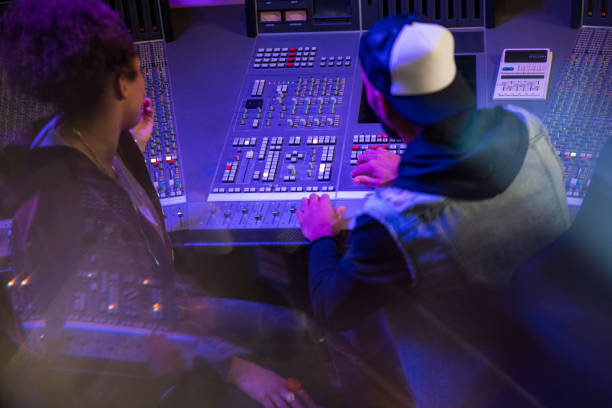 istock Back view on two musicians sitting at audio mixing control panel in recording studio. 1312158977
