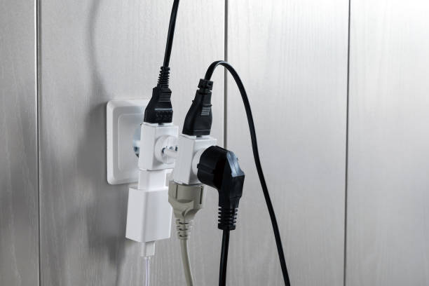 Multiple plugs in wall electrical outlet is dangerous overload, close-up Multiple plugs in wall electrical outlet is dangerous overload, close-up with copy space overflowing stock pictures, royalty-free photos & images