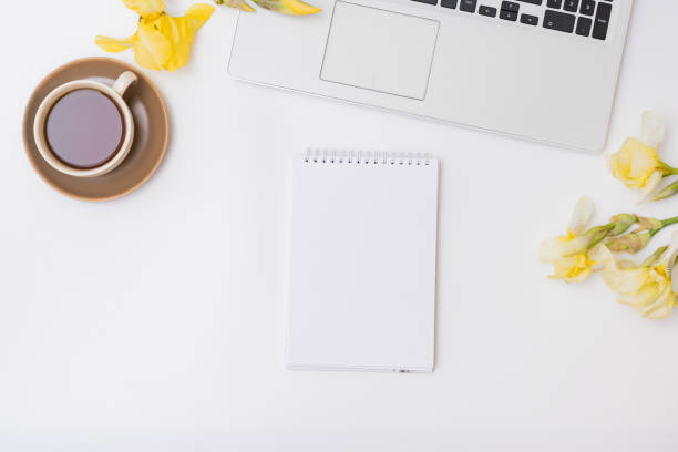 istock Flat lay home office desktop with laptop, notebook, yellow irises, cup with coffee on a white background 1312162020