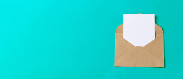 Blank white card with craft paper envelope template on green background. Flat lay, top view.