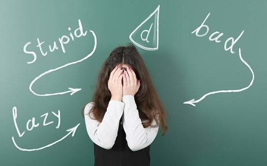 Pre-adolescent girl who just is bullied. Isolated school board background with drawn chalk  offensive words. High resolution photo. Full depth of field.