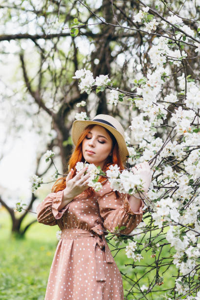 istock Red-haired girl walks in a spring blooming apple orchard 1312169911