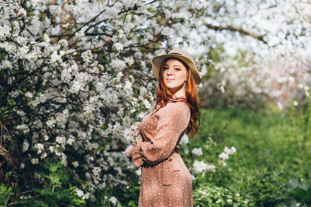 istock Red-haired girl walks in a spring blooming apple orchard 1312170956