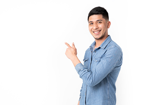 Latin man pointing finger to the side and smiling at camera with white background