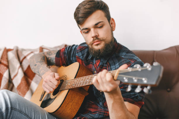 istock Young guitarist hipster at home sitting playing guitar serious 1312173785