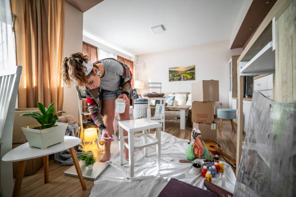 uma jovem feliz pinta e recicla uma cadeira de madeira velha para caber no ambiente de seu novo apartamento. - ambiance - fotografias e filmes do acervo