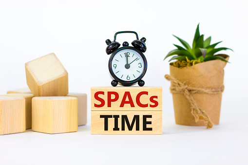 SPACs time symbol. Wooden blocks with words 'SPACs, special purpose acquisition companies time' on beautiful white background, copy space. Black alarm clock. Business and SPACs time concept.