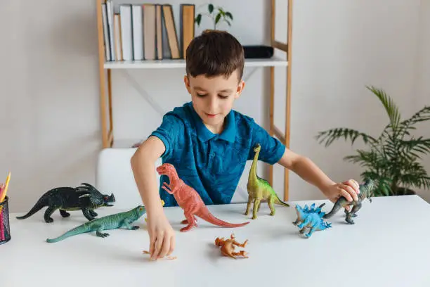 Photo of Focused kid playing with dinosaurs at home. Boy learning paleont