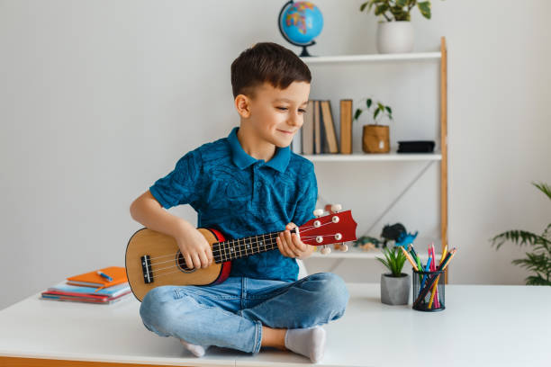 istock Talented kid playing soprano ukulele sitting on desk 1312181795