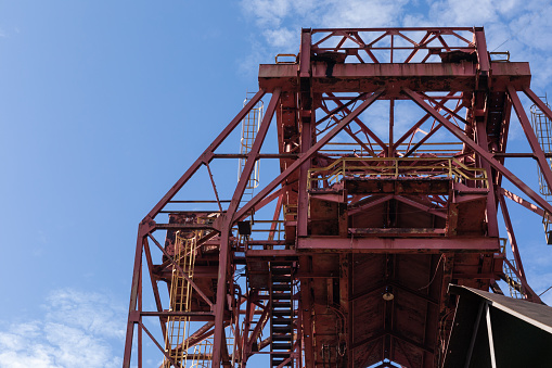 Huge rusting overhead industrial metal structure, caged ladders, blue sky, horizontal aspect